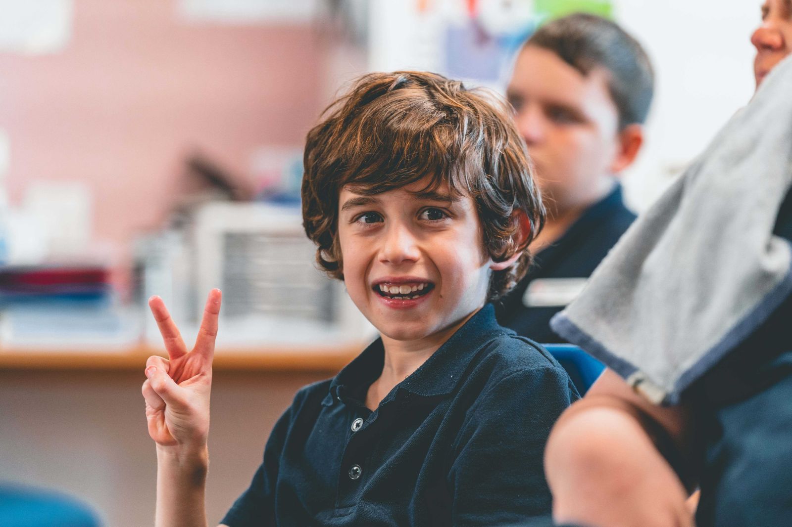 A student smiling brightly and showing the peace sign with his hand